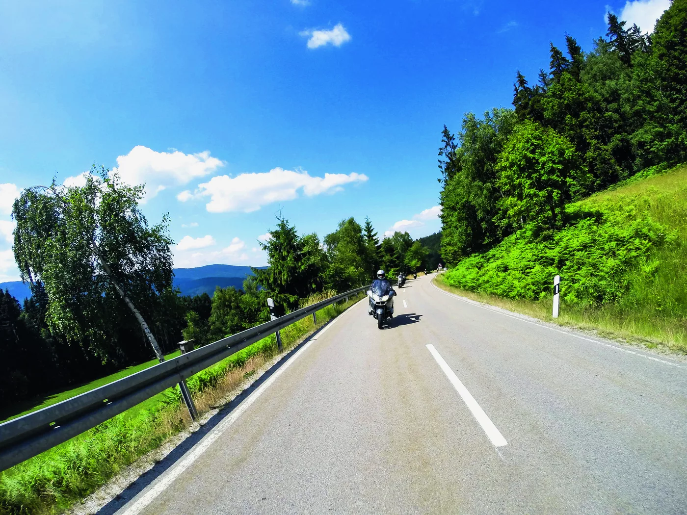 Motorrad auf einer Straße durch die bewaldete Hügellandschaft Motorrad auf einer Straße durch die bewaldete Hügellandschaft