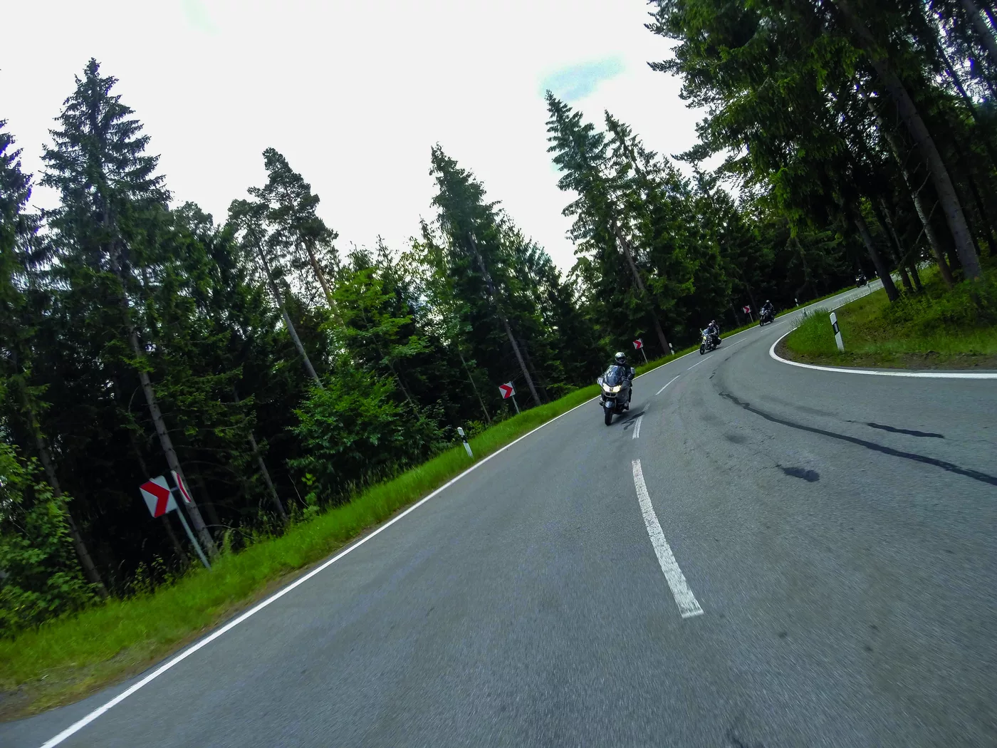Motorrad in einer Kurve auf einer Straße durch dichten Nadelwald Motorrad in einer Kurve auf einer Straße durch dichten Nadelwald